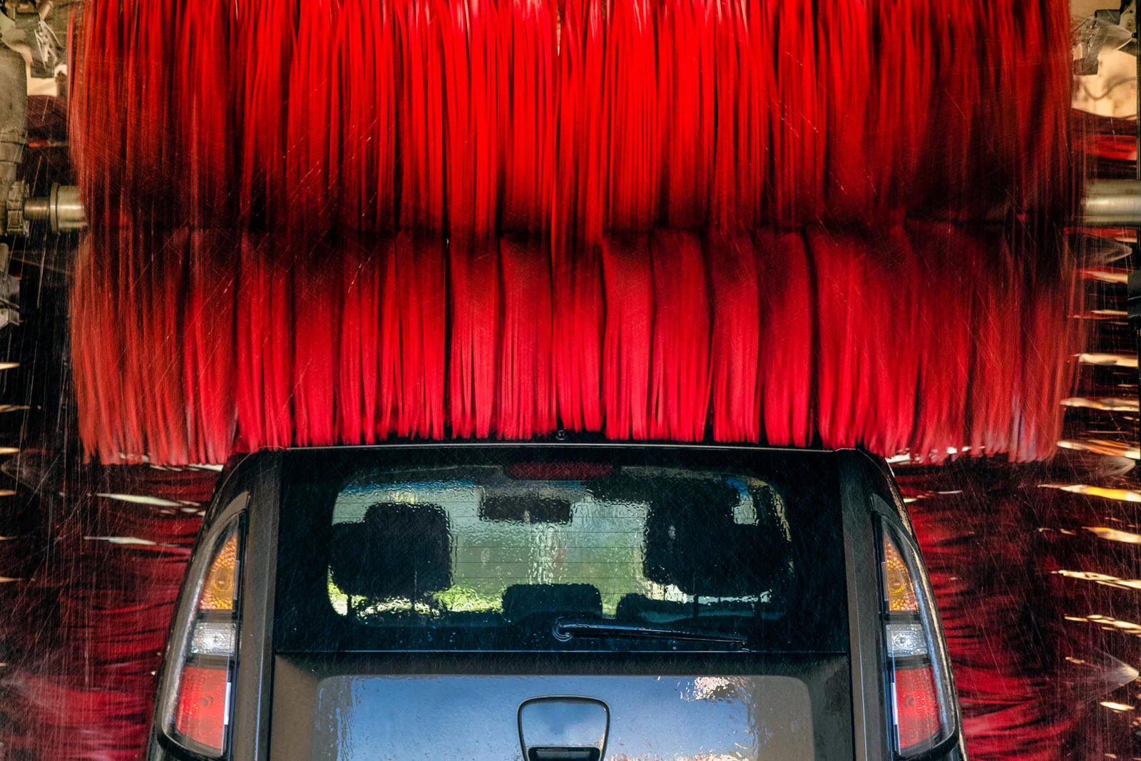 Vehicle passing beneath red brushes in an automatic car wash